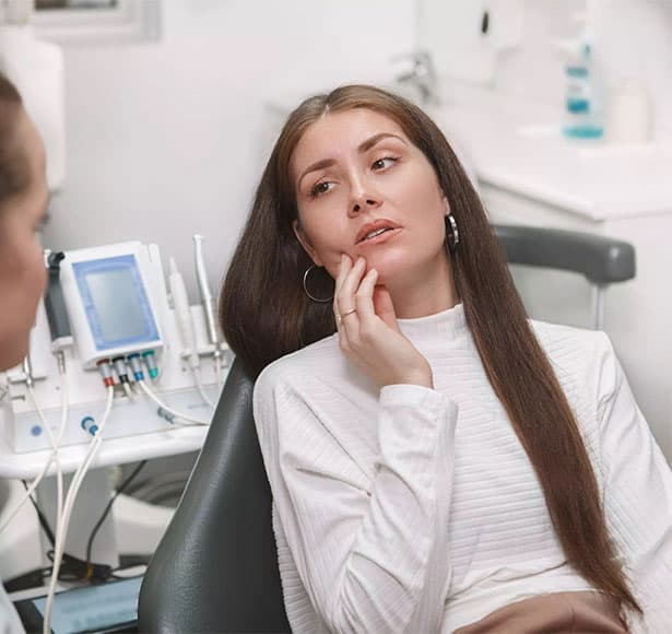 Woman holding her cheek while seated in a dental chair